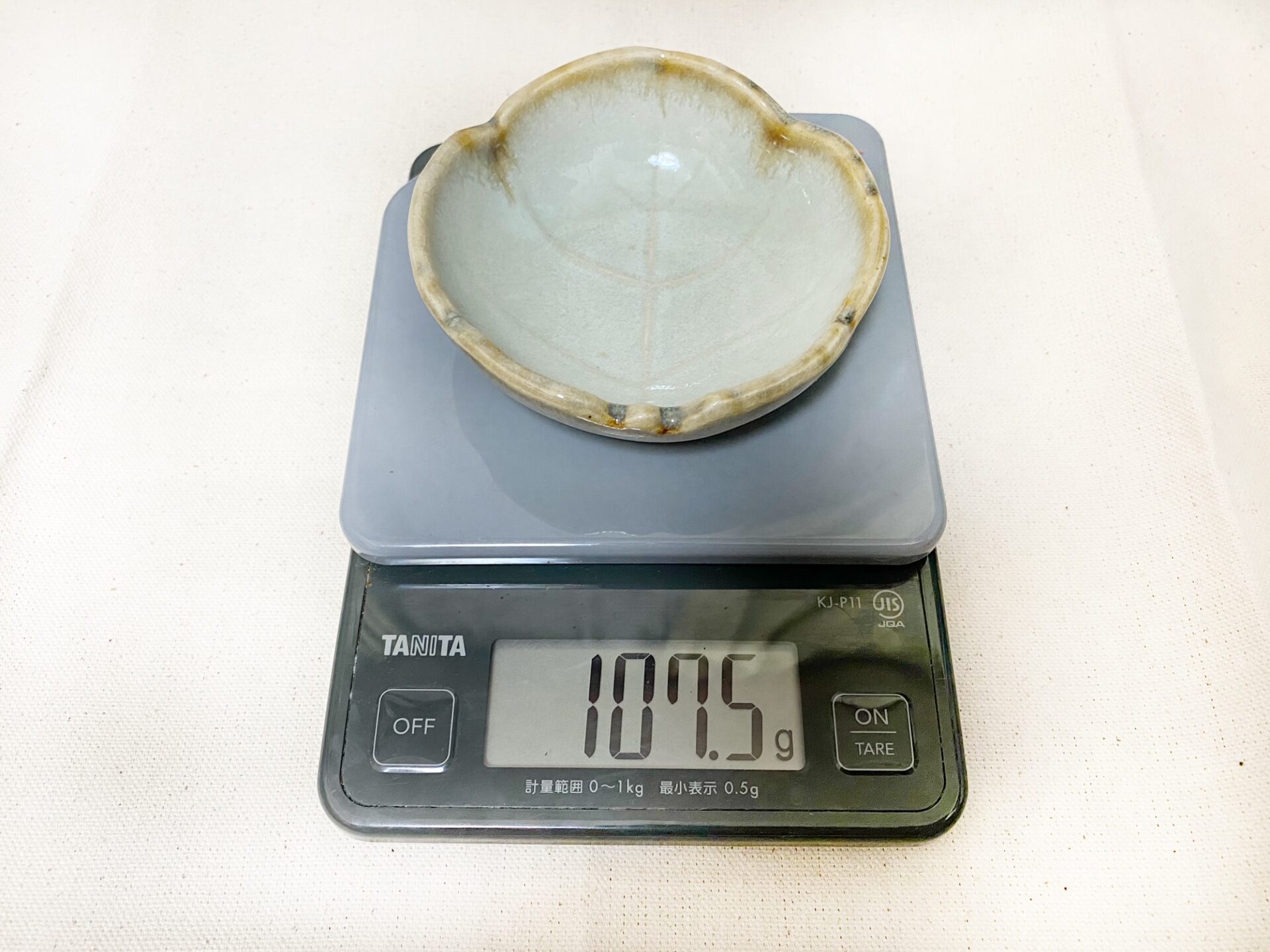 クッキングスケールの計量皿に小さいお皿をのせた写真。１０７.５グラムと表示されています