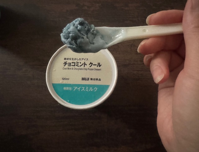 カップのふたと、スプーンですくったチョコミントクールの写真。背景が茶色いのでやや暗いですが、あきらかにまっさおです