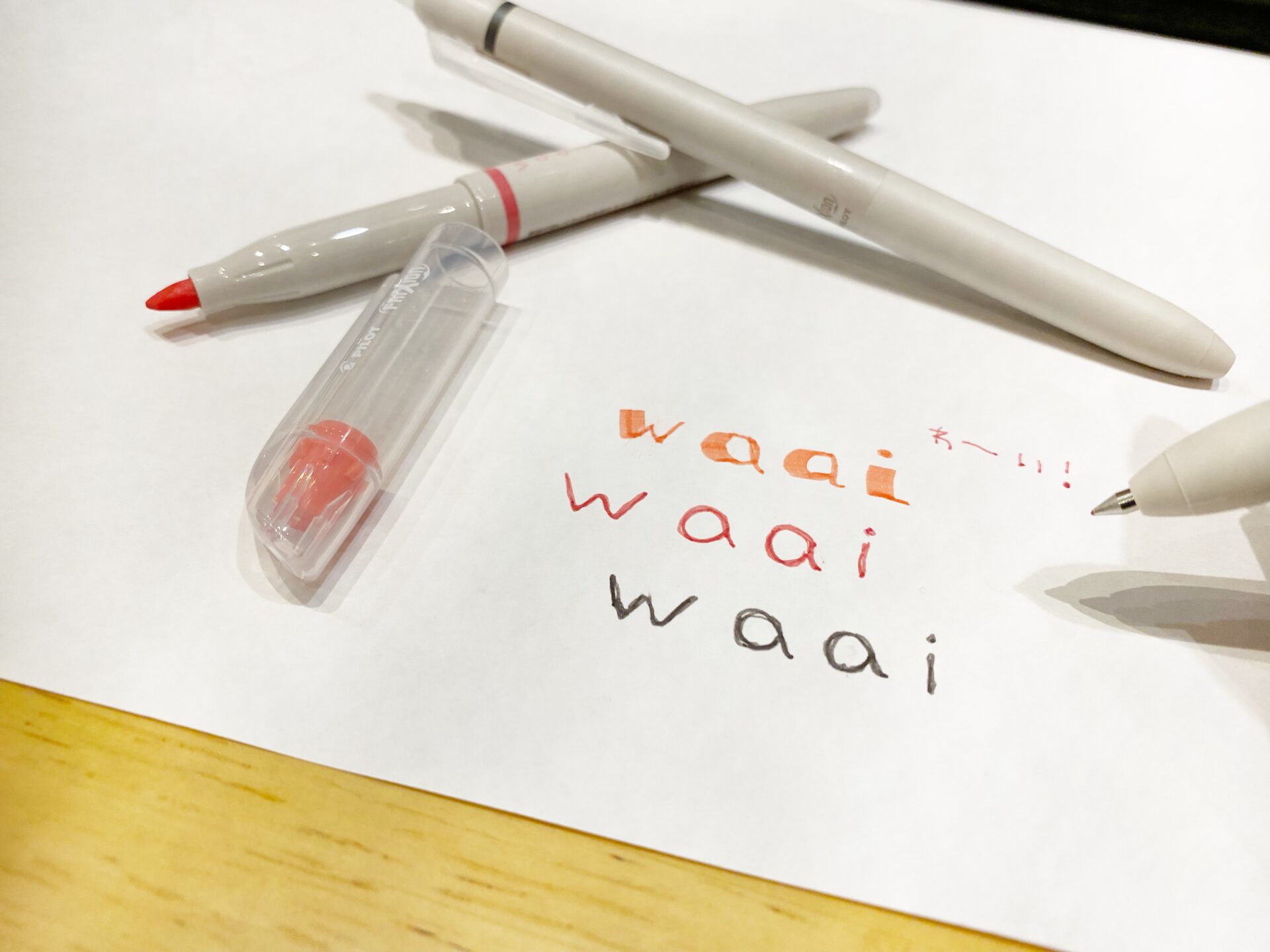 フリクションワーイのボールペン、マーカーで、白い紙にワーイのロゴを書いた写真。失敗しても消せるのが特徴のボールペンとマーカーです