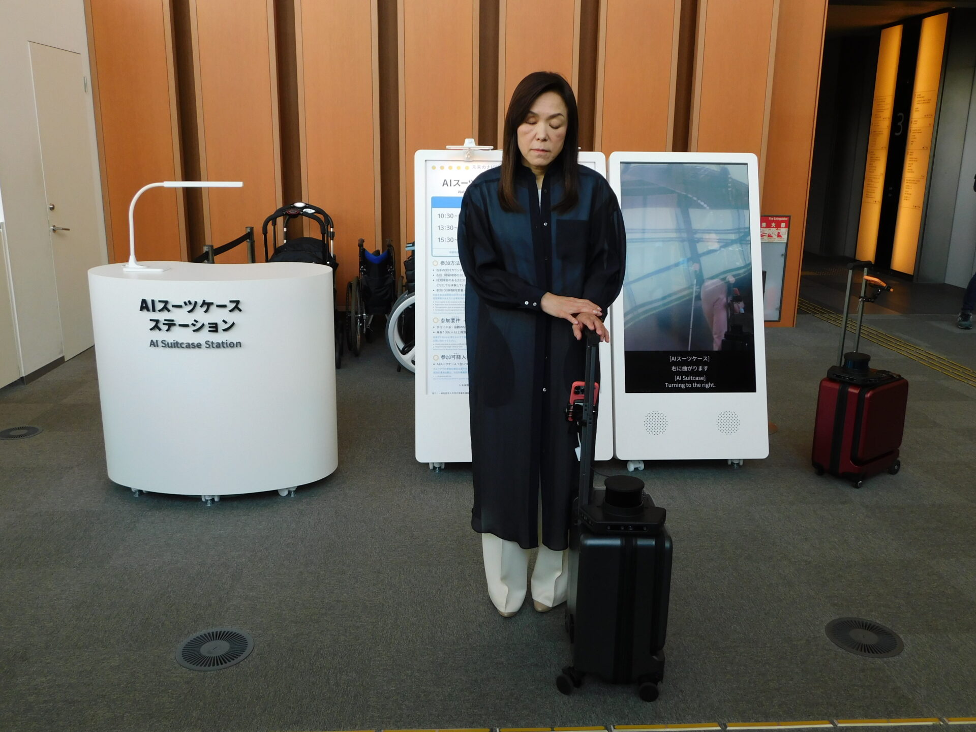 エーアイスーツケースステーションにいる、浅川館長とエーアイスーツケースの写真。エスカレーターをのぼって3階にすすみ、ひだりがわにあります