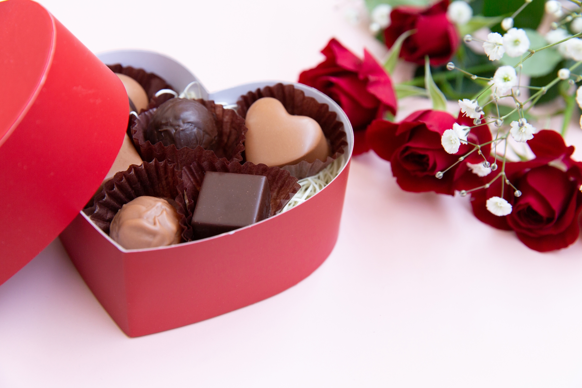 テーブルの上に置かれたバレンタインのチョコレートとバラの花。ハート型の箱の中には６粒のチョコレートが入っています
