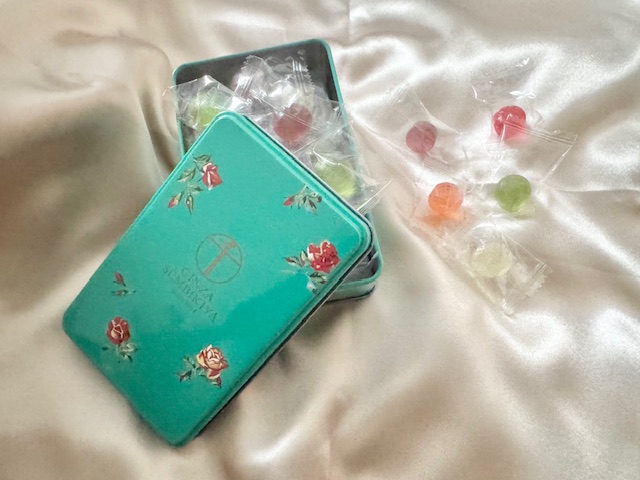 せんびきやの銀座ミックスキャンディの缶の写真。こちらも缶わエメラルドグリーンがベースで赤と白がまじったバラがところどころ描かれており、レトロで上品な感じです。個包装のふくろにひとつぶずつアメがハイっています