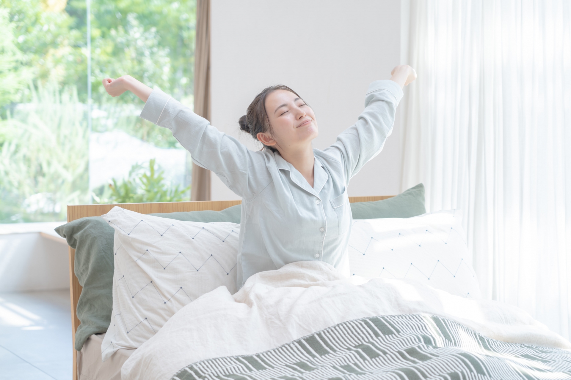 シャキッとめざめる女性。ベッドの上で両手をあげてからだを伸ばしている