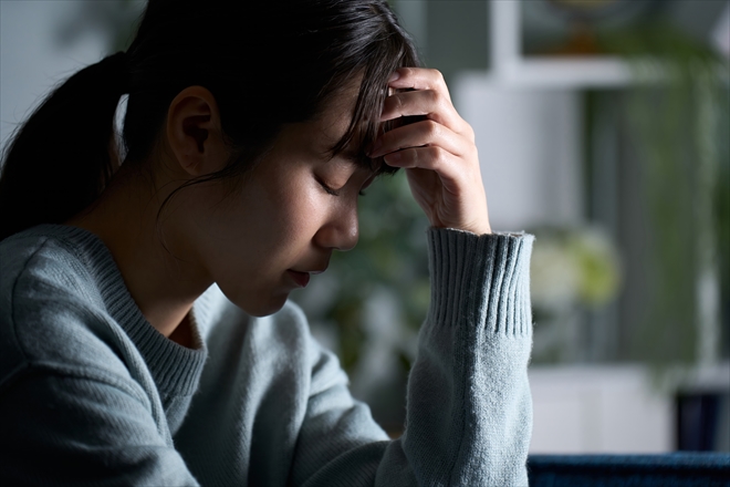 暗い部屋でひたいに手をあてて、ふさぎこむ若い女性の写真です