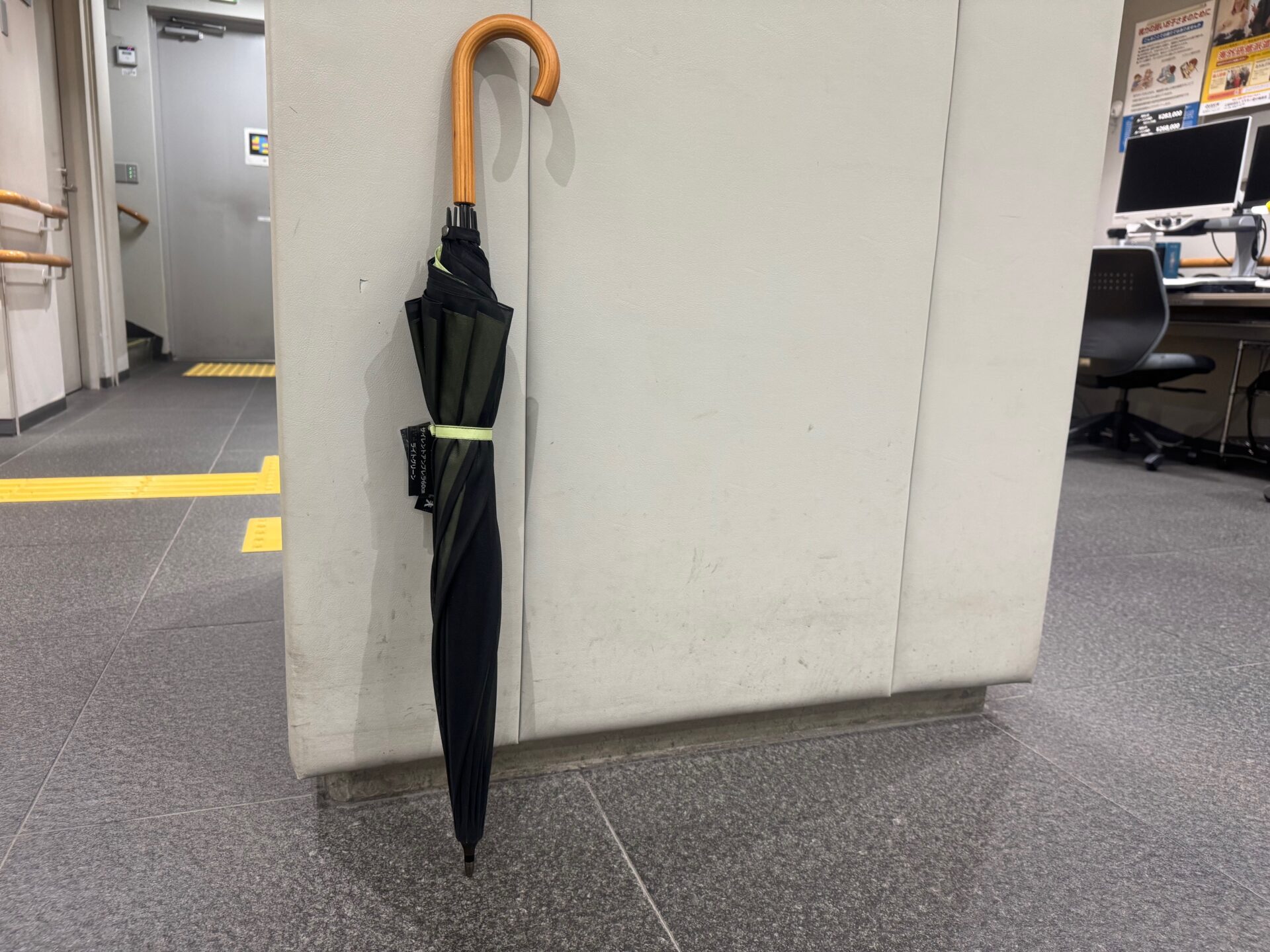 日本点字図書館の館内で撮影した、たたまれた状態のサイレントアンブレラの写真。グリーンのシンプルなきじのうえに、シースルーのくろいきじがおしゃれです