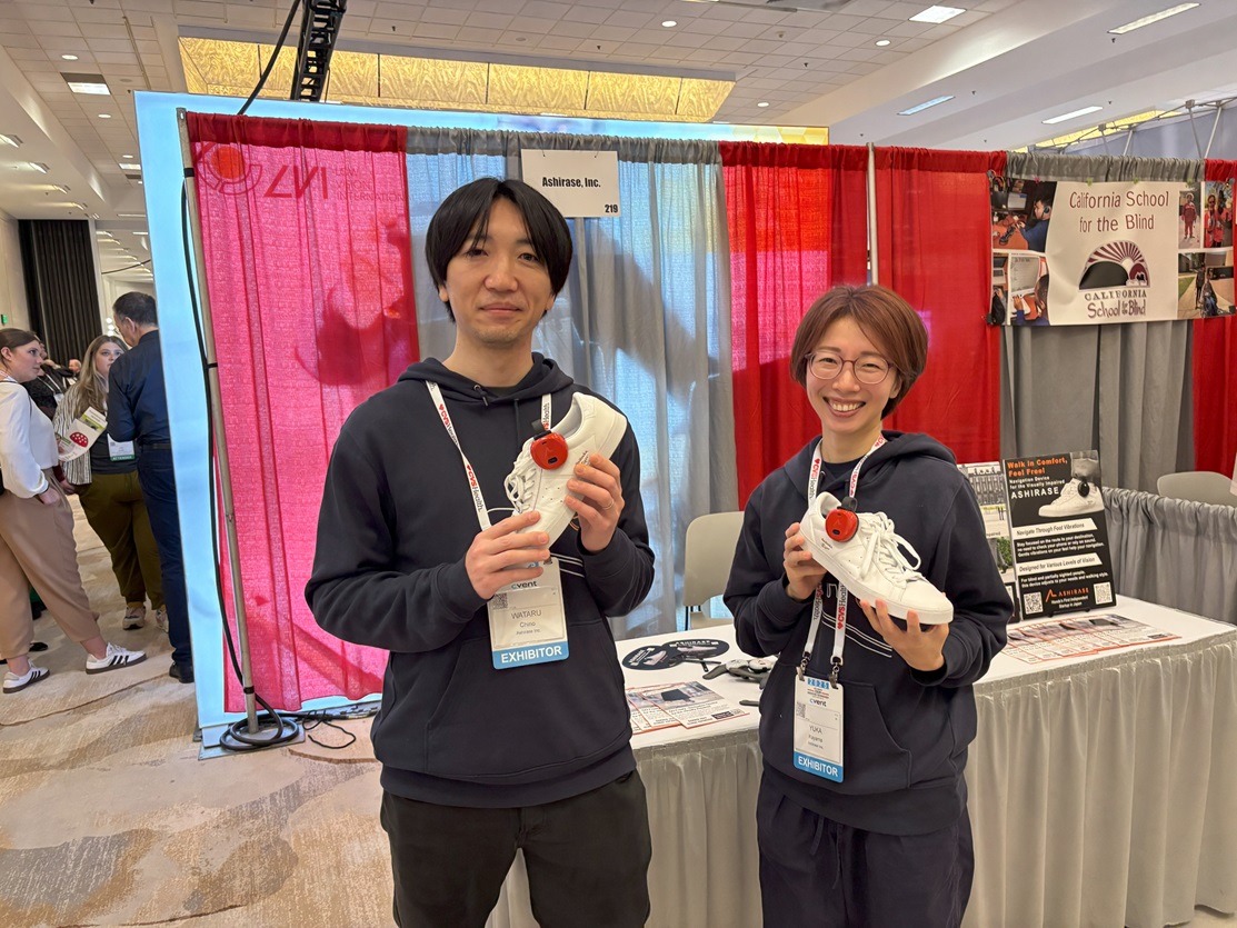 あしらせのブースの前で、あしらせをつけたしろいスニーカーをそれぞれ手に持ってほほえむ千野さんと香山さんの写真。とくに香山さんは数日前までスペインにいたとは思えないさわやかな笑顔です