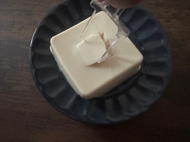 とうふこばちスプーンで豆腐を掘っている様子をうつした写真。きれいに惚れると四角い穴があきます。そこに醤油をたらしたりもりつけをするときれいにしあがるというわけです