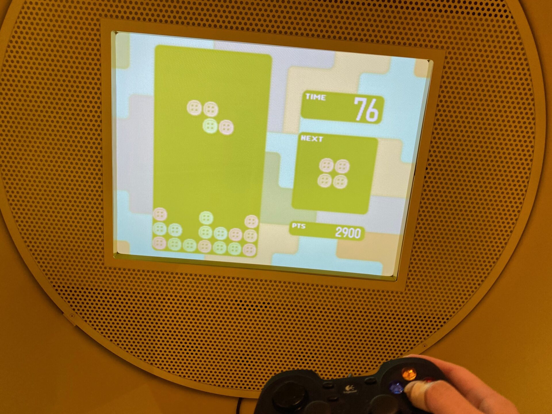 「3つのまるまるなテレビゲーム」で遊んでいる様子の写真。手元のコントローラーをつかって上から落ちてくるかたまりのブロックの向きや位置を変えながら積み重ねていき、同じ色のブロックが4つ続いたら消去できるゲームなのですが、黄色みがかってみえるので異なる色も同じ色のように見えてなかなか思うようにブロックが消せません