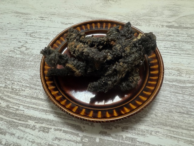 ちゃいろいおさらにのった、ブラックのゲソてんの写真。ころもわいかすみのようにマックロです