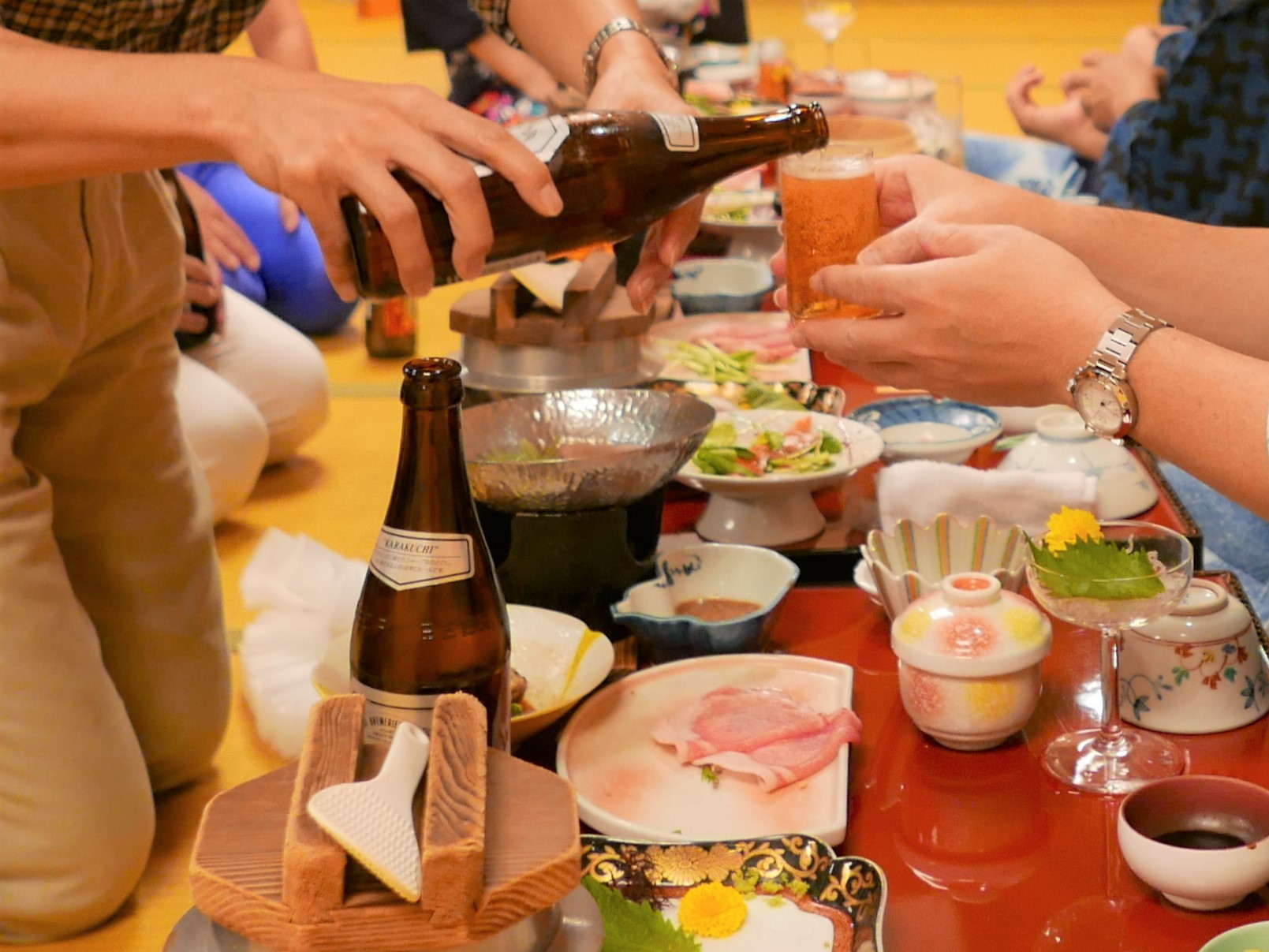 テーブルにたくさんの料理やビールなどが並んでいる忘年会の写真です。手前の席ではビールをお酌する光景も散見されます