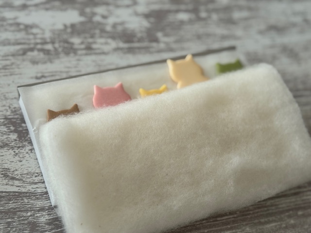パッケージを少しだけフォーメーションチェンジし、5匹のねこをわたのおふとんに寝かせたように写した写真。ねこのみみだけだったり、あたまだけでたねこさんがかわいいです