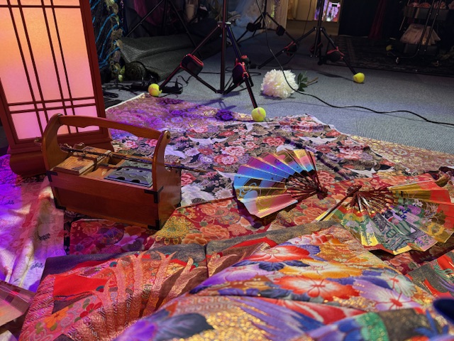 ビビッドで豪華な着物のような柄の布のうえに、キセルやせんすふたつがむぞうさに置かれている写真