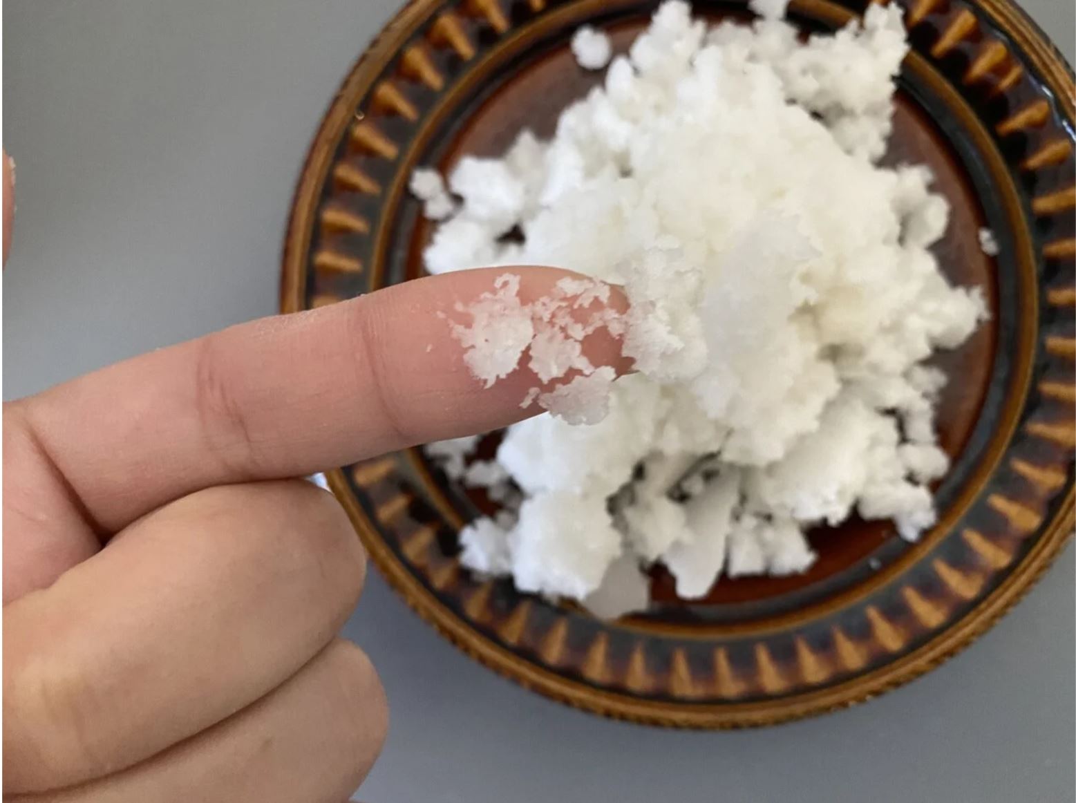 指にのせた塩の写真。背景には小皿にのったまっしろな塩がうつっています