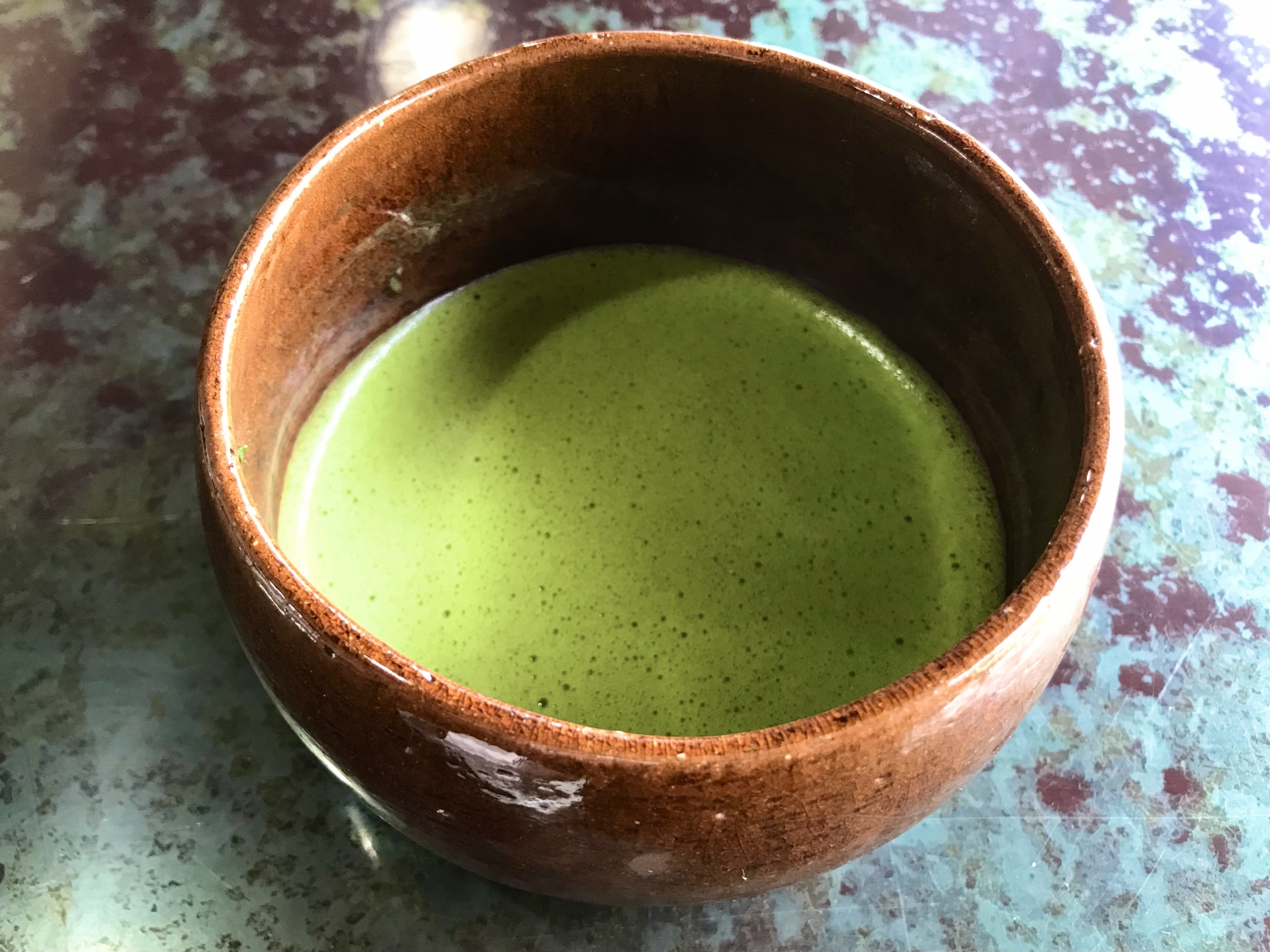 抹茶の写真です。茶色いとうきに緑色の抹茶が入っています。茶の表面はうっすらと泡で覆われています