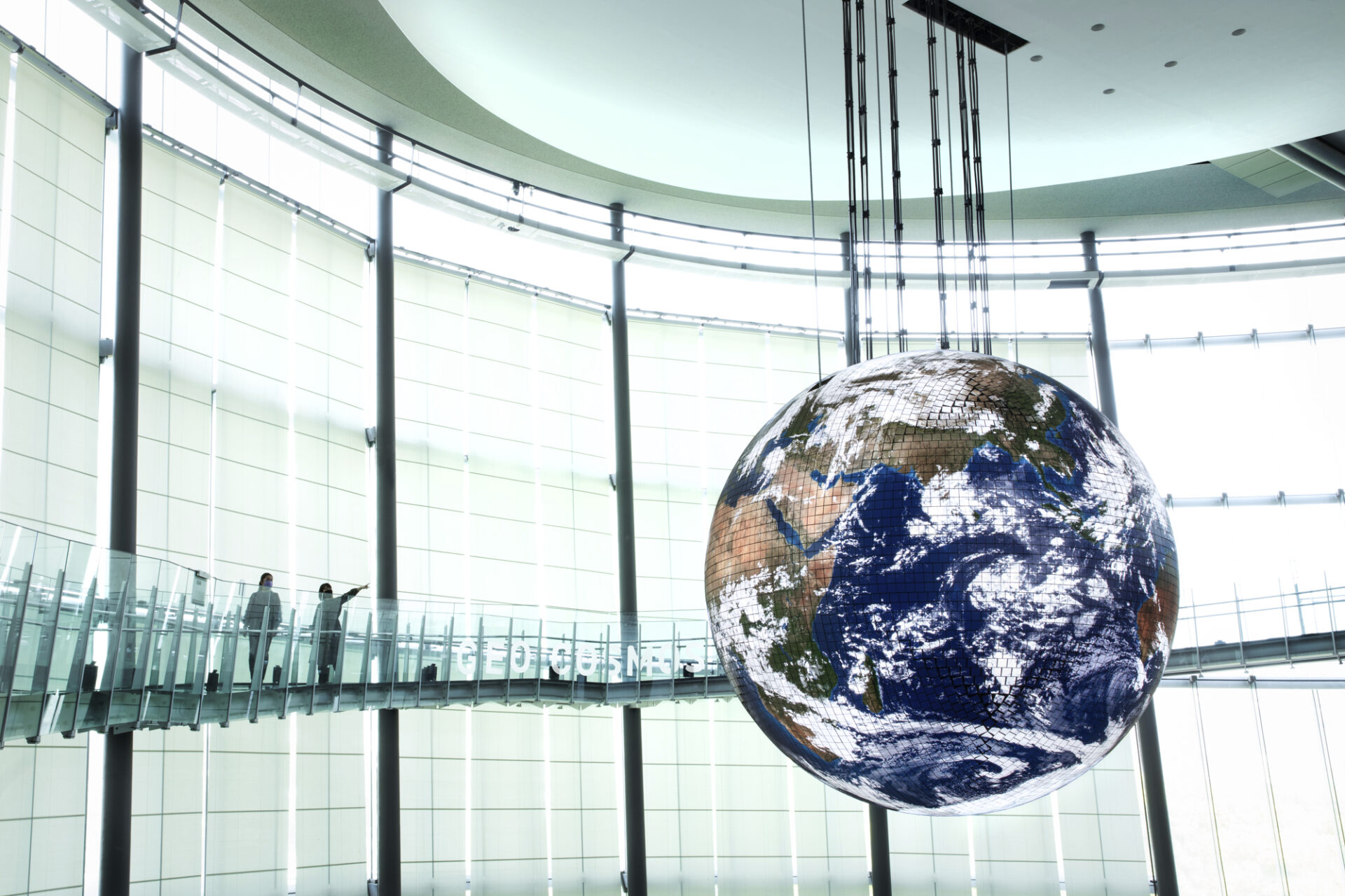 ②代替テキスト:未来館のシンボル展示「ジオ コスモス」の写真。吹き抜けの大きな展示空間に大きな青い地球が映し出された球体が浮かんでいる様子が見えます。