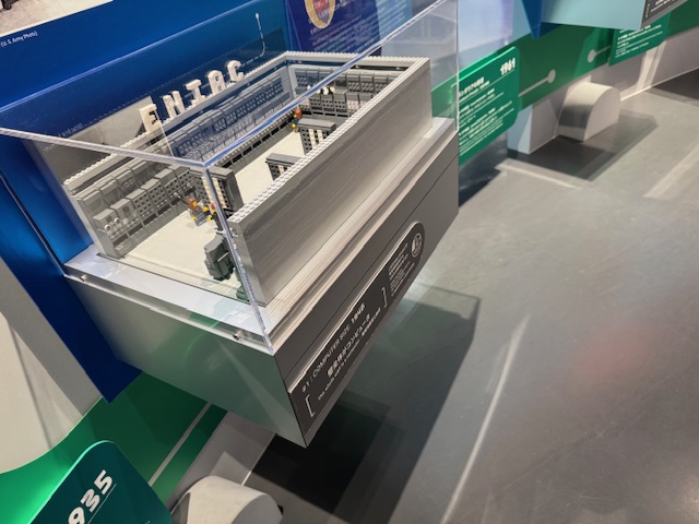 むかしのコンピュータの様子をレゴブロックをつかって展示した様子。部屋いっぱいにコンピュータが並んでおり、そのなかに人がいます。まるで部屋がまるごとコンピュータのようです。壊れないようにガラスのケースにハイっているため、こちらはさわることができません