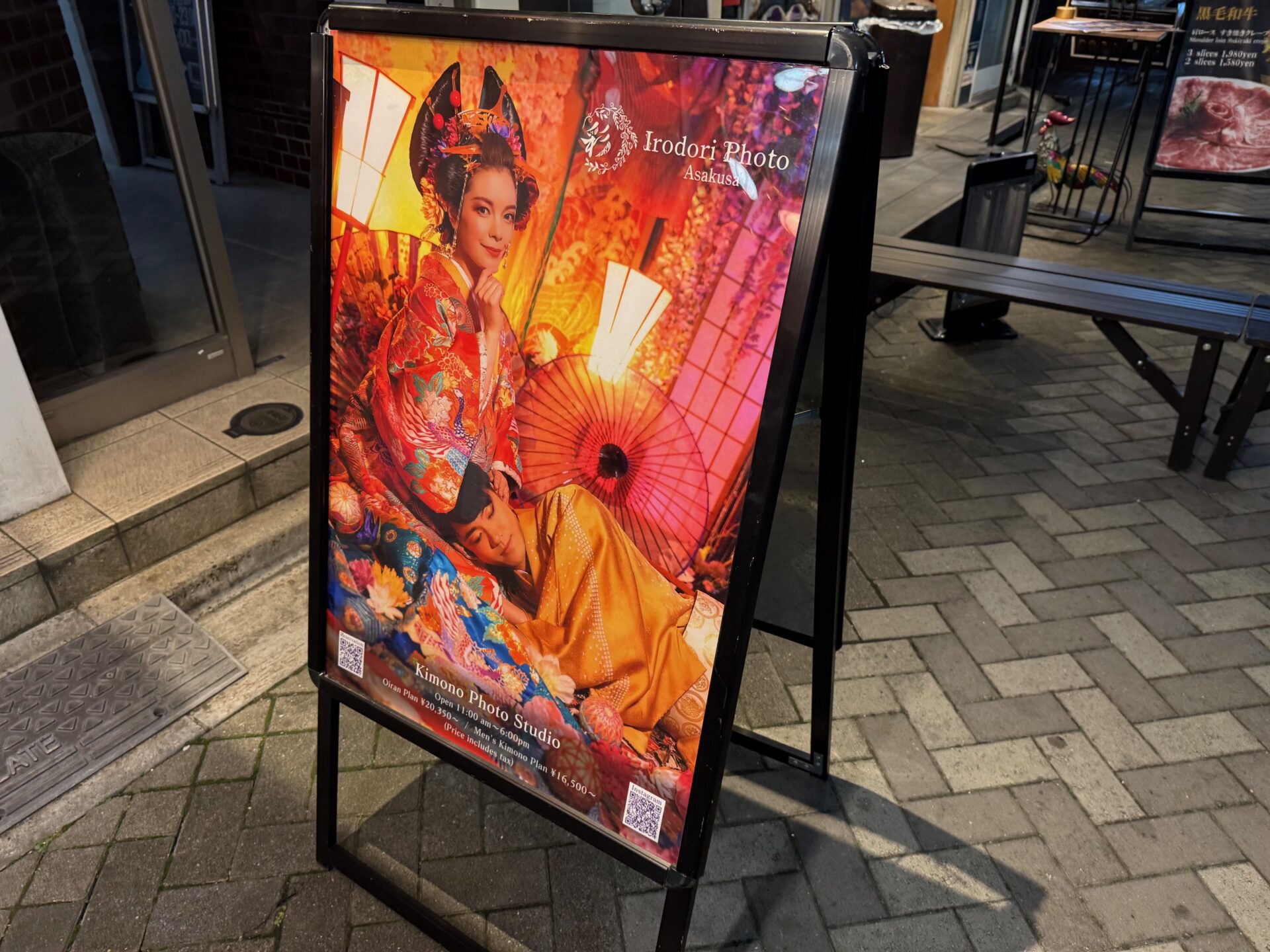 ビルのそとに置かれた、お店のおき看板の写真。きらびやかなおいらんに変身した女性と、そのひざもとで眠る男性がうつっています