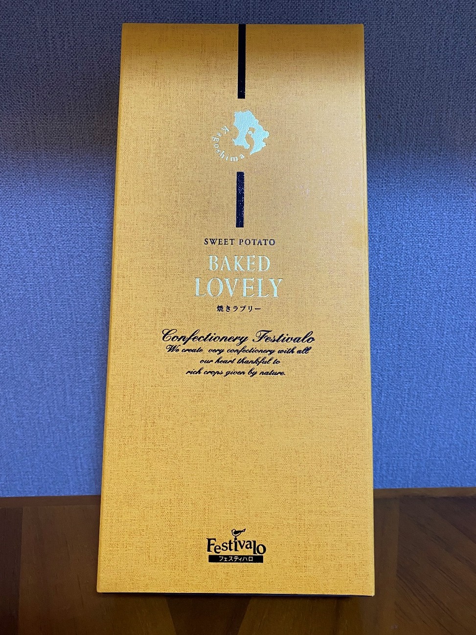 金色の箱の上部に銀色で「KAGOSHIMA」というロゴが記載されてあり、中央に「SWEET POTATO BAKED LOVELY　焼きラブリー」と書かれています。その文字の下部には、黒色の筆記体で「Confectionery Festivalo」とあり、その下に「We create very confectionary with all our heart thankful to rich crops given by nature」という英文が続きます。箱の一番下には「Festivalo」というロゴがあります。