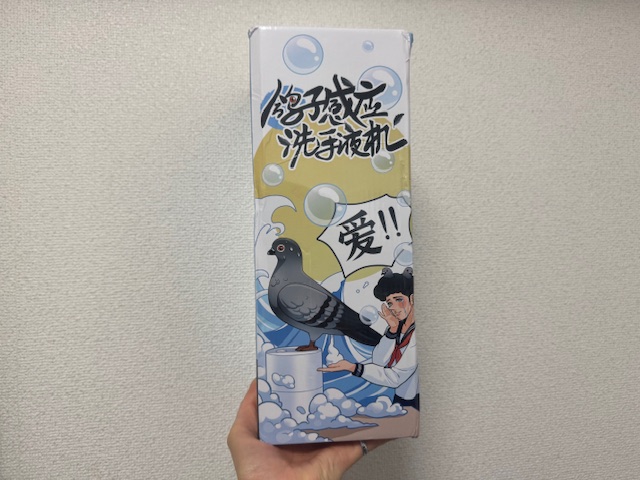 鳩が乗ったハンドディスペンサーと、あらやだかわいいという表情をした女性のコミック調のイラストが描かれた、りっぽうたいの紙製のパッケージを手で持った写真。文字も書いてありますが中国語で読めません