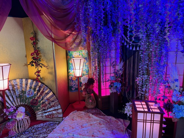 撮影用の背景の写真。左がふじの花がたれさがっており、青いライトに照らされながらムード満点に。みぎがわわゴールドのびょうぶにライト、せんす、お面など、撮影ちゅうにからだの向きを変えるだけで屋外と屋内それぞれの写真がとれるようになっています