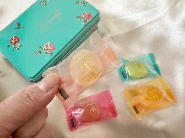 4種類の個包装のグミを並べた写真。そのうちひとつを手でもっています。背後には缶も映り込んでいます