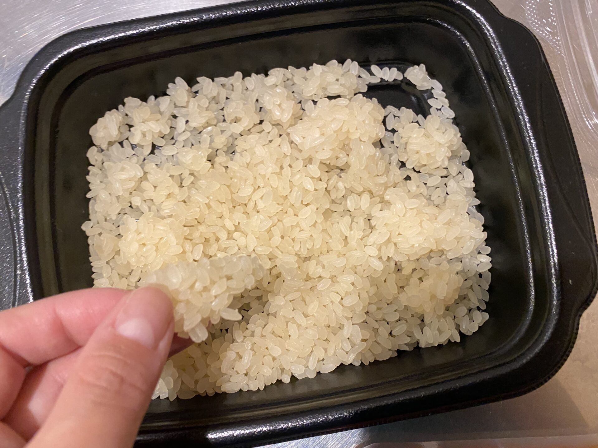 容器に袋から出したお米を入れた写真。かたまりになったお米を指でもちあげています