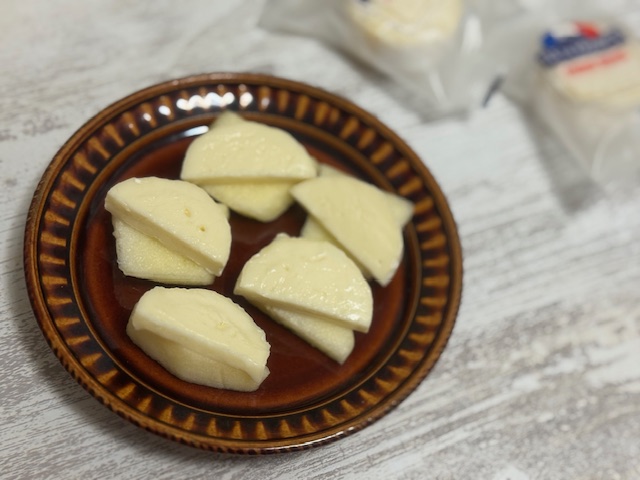 ちゃいろくてまるいお皿にのった、うすくきったカットりんごのうえに、こちらもうすくきってハンゲツぎりにしたミニブリーをのせたものがいつつのった写真。背景には個包装になったミニブリーがふたつ映り込んでいます