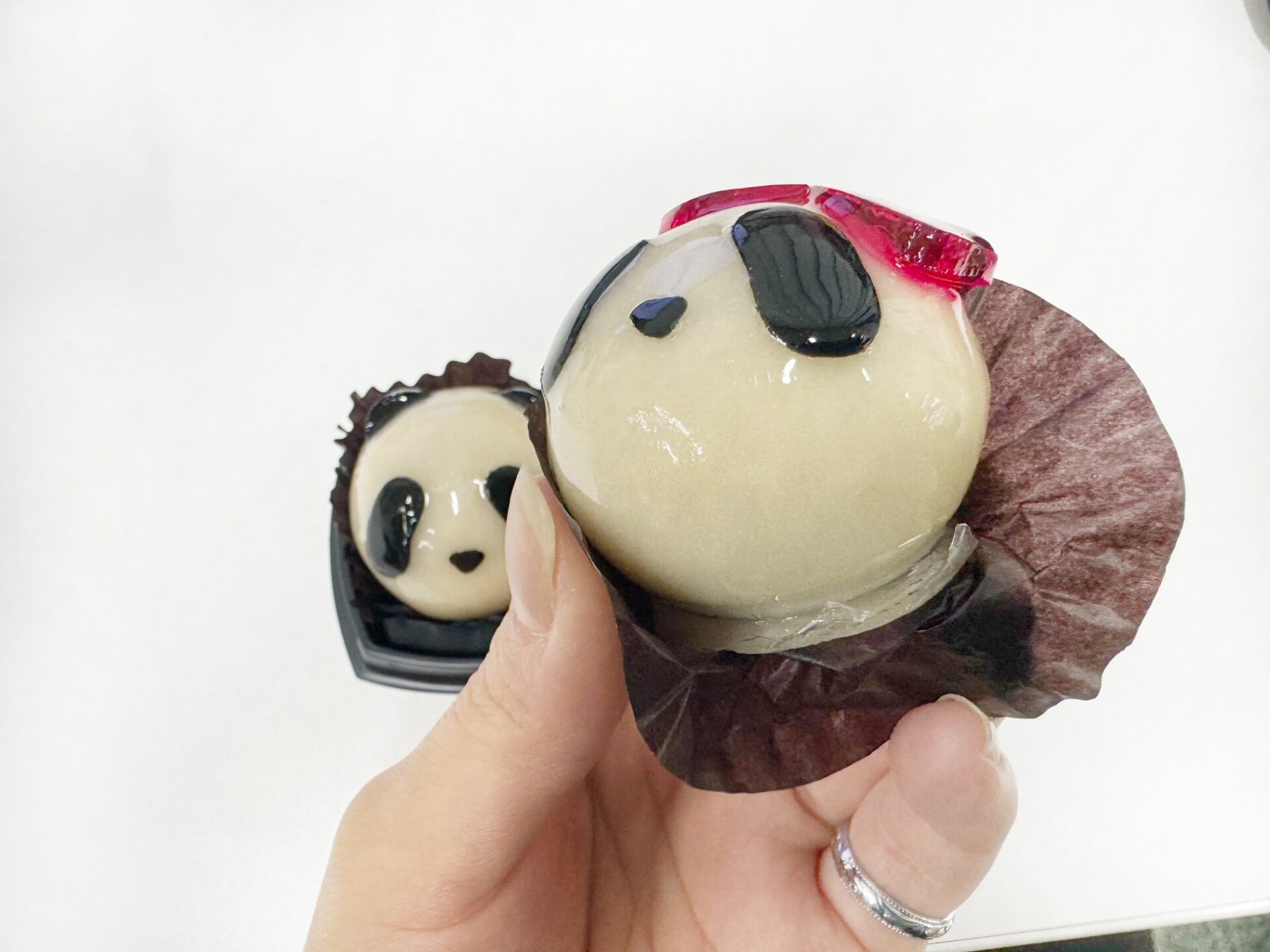 メスのパンダのあんだまの紙のつつみをとちゅうまでハガシた、食べるちょくぜんのあんだまの写真。パンダがたれ目だからか、アングルてきに「たべちゃうの?」と悲しそうな目をしているようにみえてきます。しかも背景にうつりこんでいるオスのパンダも「たべないであげて」と言いたそうな目にみえてきてしまい、食べるのが若干きまずい雰囲気になっています