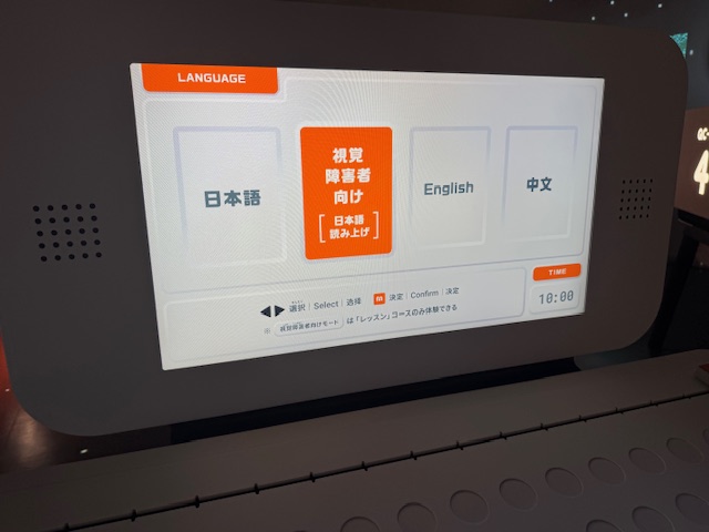 ダンスフロアの体験機器のモニターの写真。モニターには日本語、英語、ちゅうぶん以外に、日本語読み上げ対応の視覚障害者向けモードがあります