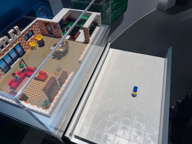 レゴブロックでつくられた70年代のコンピュータのジオラマと、さわってわかるレゴブロックの写真。大きな部屋の中央にぽつんとひとつだけ、青いレゴブロックが設置されており、そのとなりに人間型のレゴブロックが配置されています