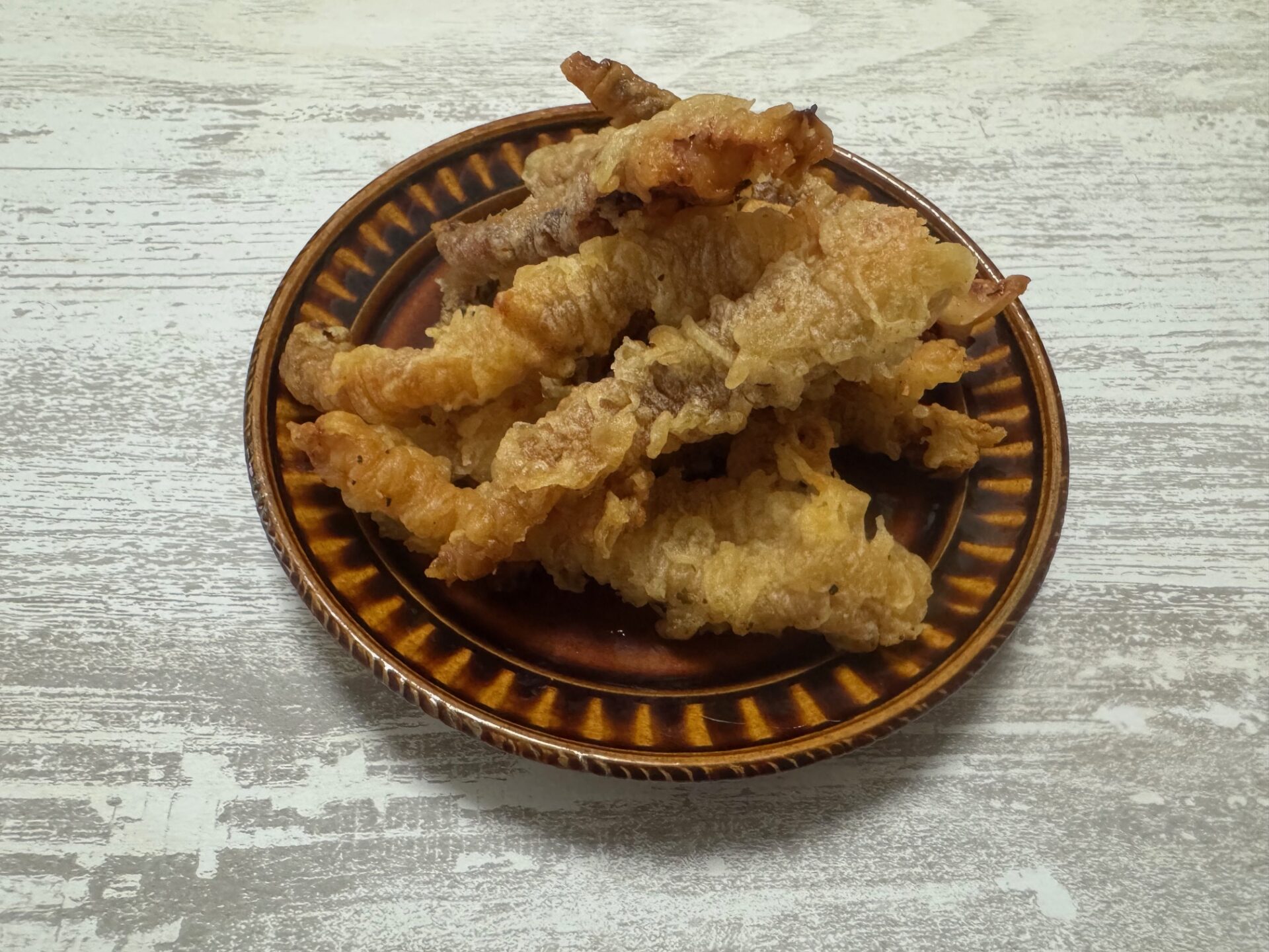 ちゃいろいおさらにのった、レモンのゲソてんの写真。ころもわいつもの天ぷらとおなじようないろです