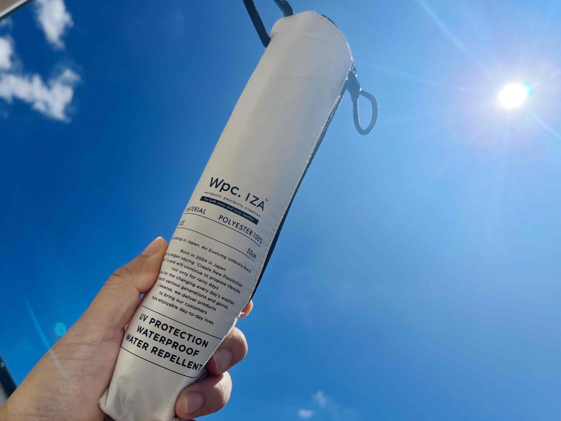 wpcイーザの折り畳み傘を手にもって青空にかざしている写真。太陽がまぶしいです