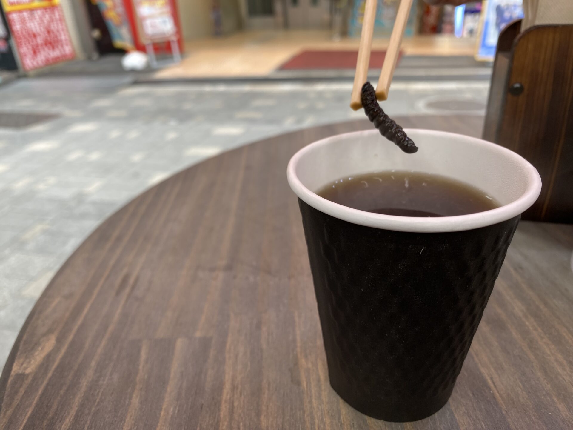 サクラケムシ紅茶のなかからケムシを箸でとりだした写真。すうせんちていどのありのままのすがたのサクラケムシのしろっぷづけが１匹ハイっている
