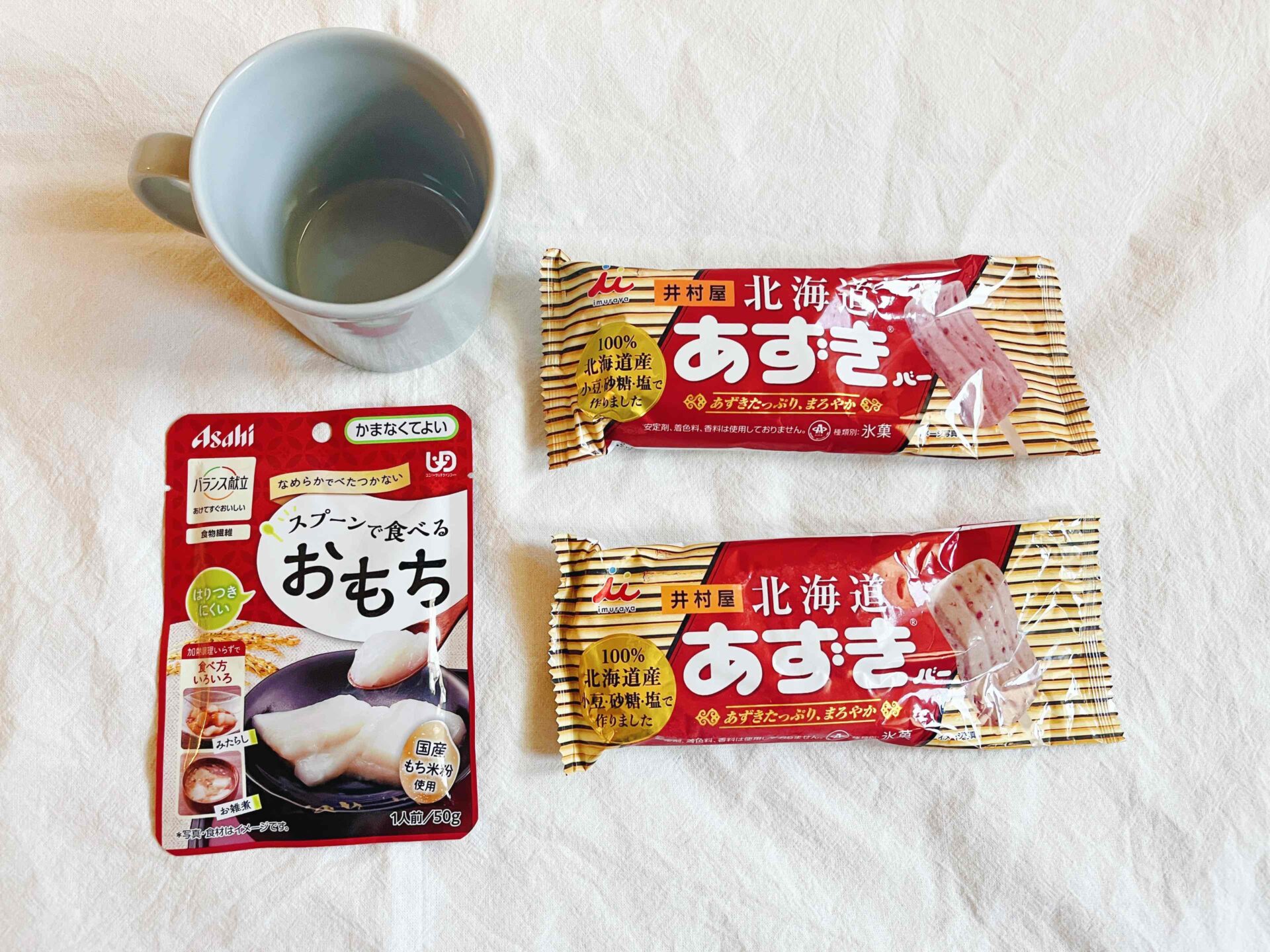 マグカップとあずきバー2本、スプーンで食べるおもちのパウチが並んでいる写真