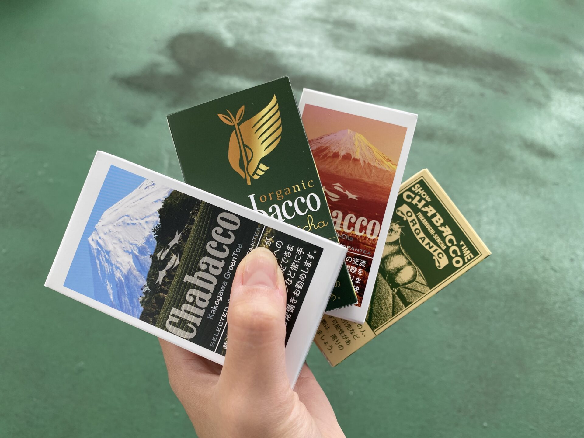 タバコのような見た目の粉末のお茶、チャバコのパッケージ４種類を手に持った写真