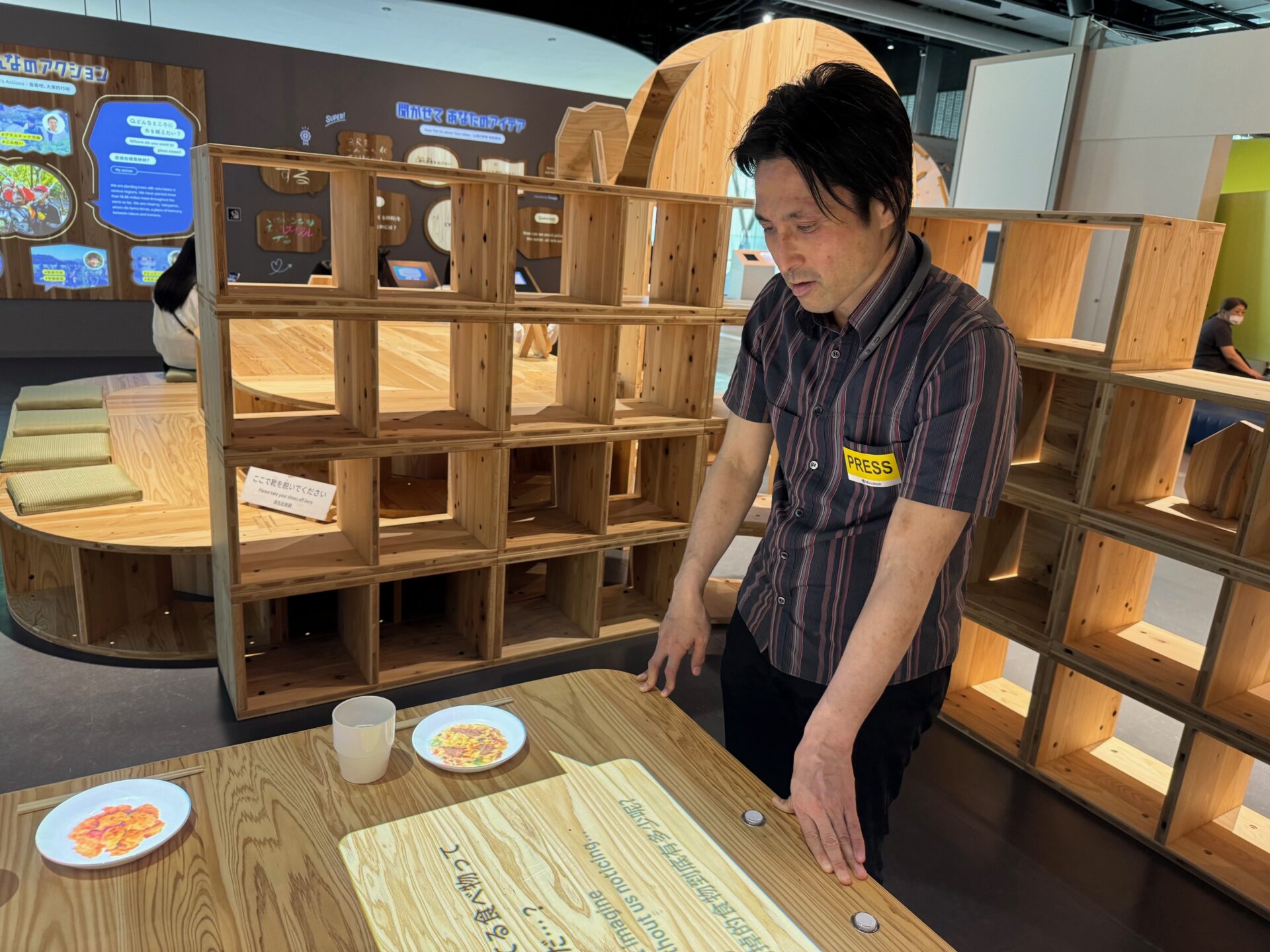プラネタリー・クライシスの展示の前でネックスピーカーから流れるガイドを聞きながら展示を鑑賞しているしらとりさんの写真