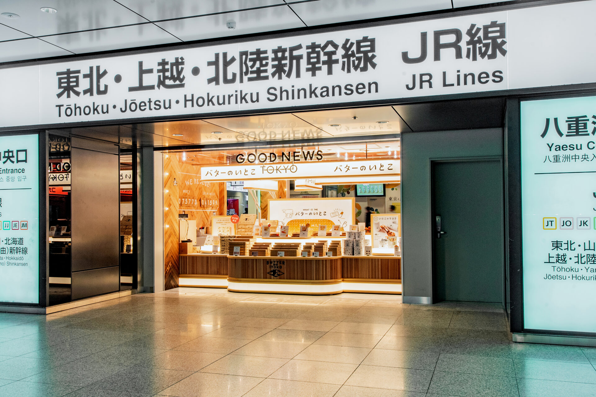 改札の外からみたグッドニューストーキョーのお店の外観写真。お店の上に「東北、上越、北陸新幹線JR線」と書かれた看板が映り込んでいることからもわかるように、東京駅やえすちゅうおうぐちの改札すぐ横にあります。テイクアウト商品がならぶコンパクトなおみせです