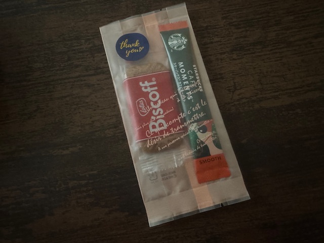 スティックタイプのインスタントコーヒーと、ロータスビスケットのセットひとつずつが透明のふくろにまとめて入れられているパッケージの写真。サンキューのシールもついているので、このままわたせます