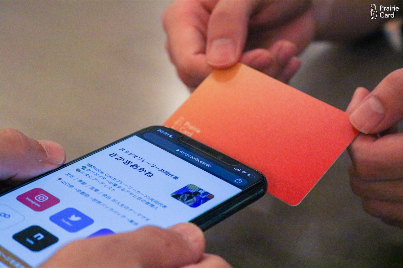 プレーリーカードにスマホをかざし、データを読み込んだふたりのひとの手元の写真。スマホの画面にはカードのもちぬしのプロフィールページが映し出されています