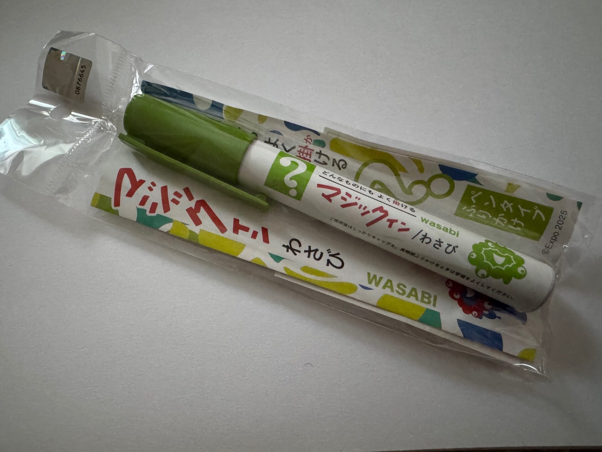 透明なほそながいふくろにハイった、ほそみのマジックインキのふりかけの写真。みどりいろのペンに似せたみためで、ミャクミャクのイラストもかかれています。ふりかけのあじわ、わさびです