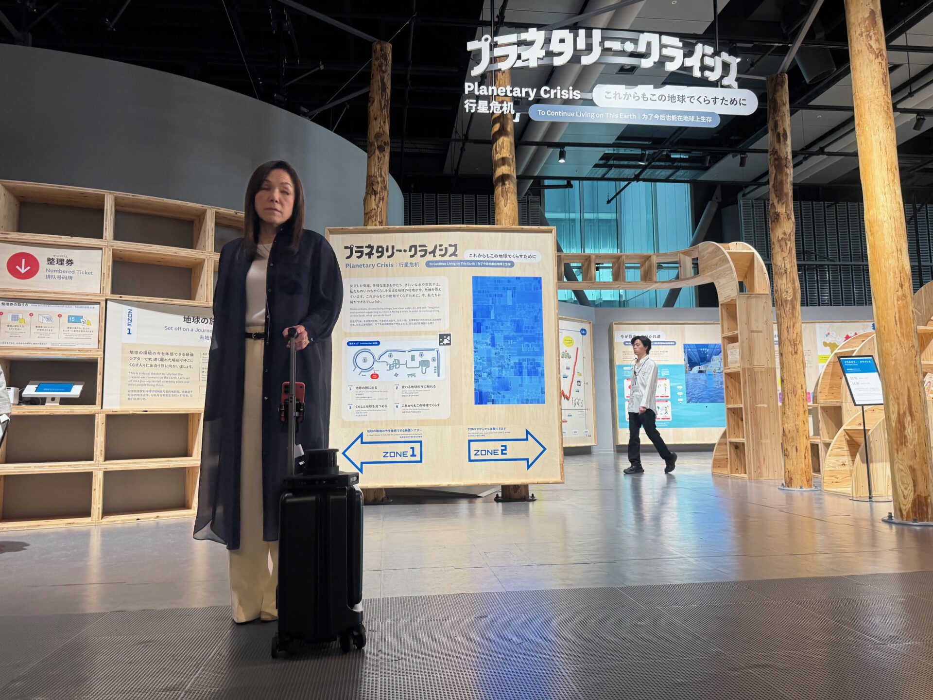 にっぽん科学未来館5階の常設展示のプラネタリー・クライシスの前で、エーアイスーツケースを持つ館長のあさかわ智恵子氏