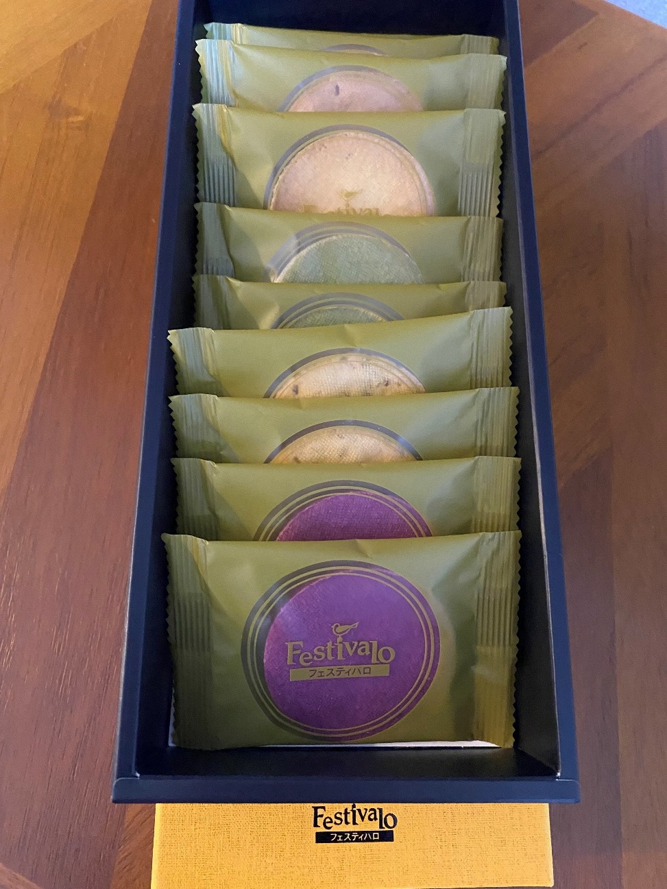 箱に入ったお菓子の詰め合わせです。箱の中には、マスタードイエローの包装紙に包まれたお菓子が縦に10個並んでいます。お菓子にはそれぞれ円形の模様があり、中のお菓子の色が透けて見えています。 