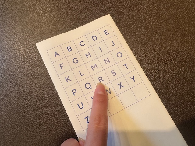 AからZまでのアルファベットと日本円のマークが書かれたページで、Rをひとさしゆびでさしている手元を写した写真