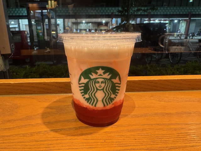 スターバックスのザいちごみるくの写真。中央にスタバのロゴがハイッタ透明なプラスチックのカップに、底にわかにくいりジャムのようなまっかないちご、そのうえにミルクがそそがれ、氷がハイッタつめたいドリンクです。ふとめのストローでかにくごとたのしめます