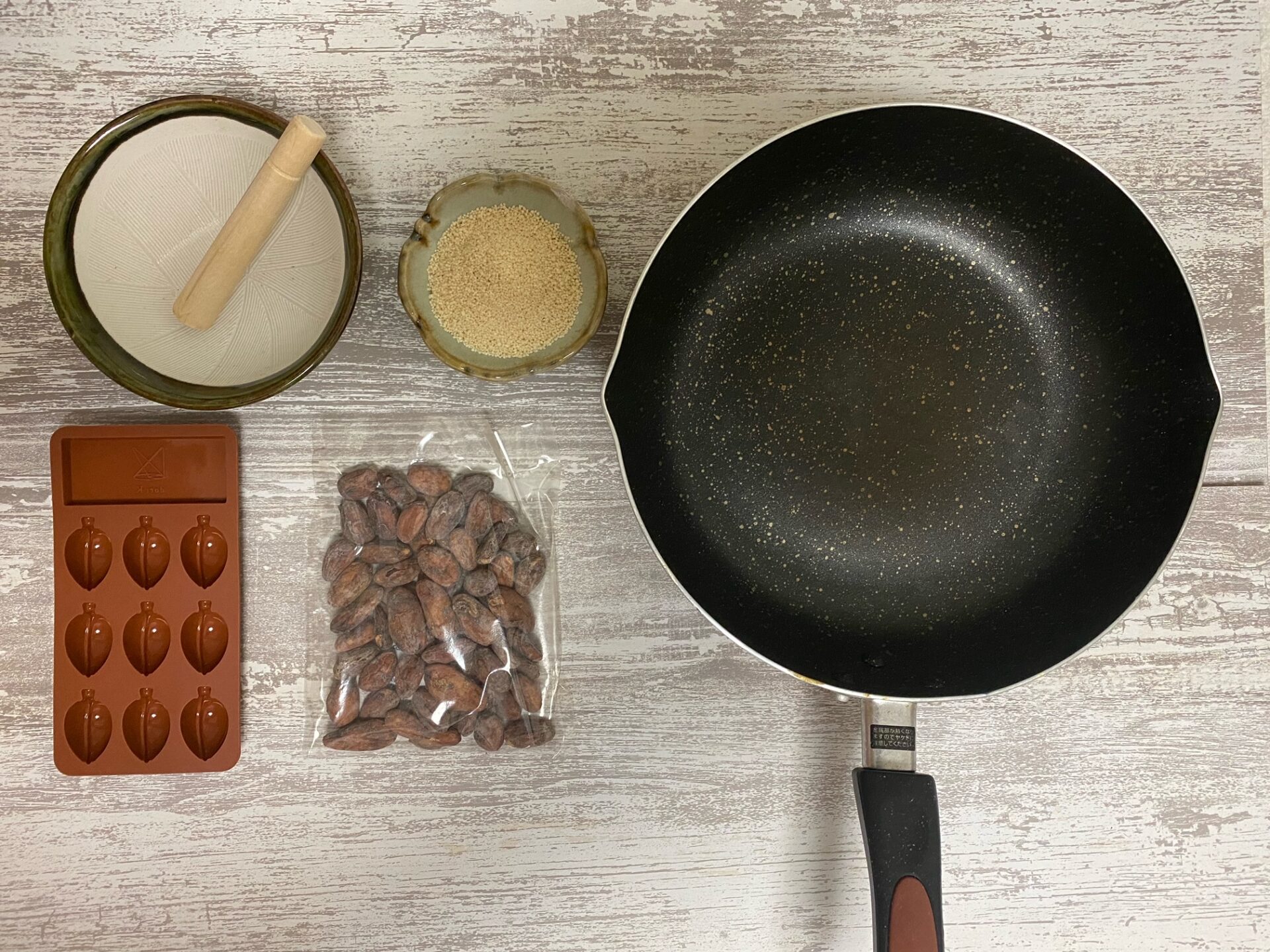 なまカカオ豆８０グラム、シリコン製のモールドがひとつ、フライパン、すりばち、すりこぎ、きび糖の写真