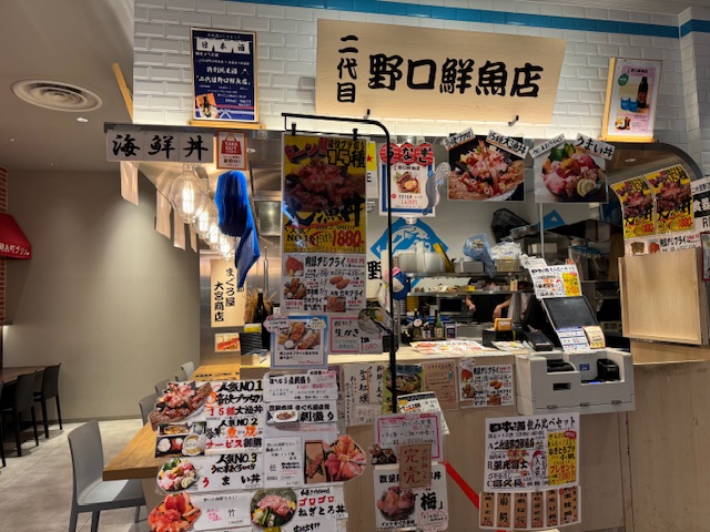 にだいめのぐちせんぎょてんの写真。写真やメニューのポップがたくさんハリだされています。さきに注文してお会計をすませ、ブルブル振動するブザーが鳴ったらカウンターまで受け取りに行くシステム。なお、レジはセルフです