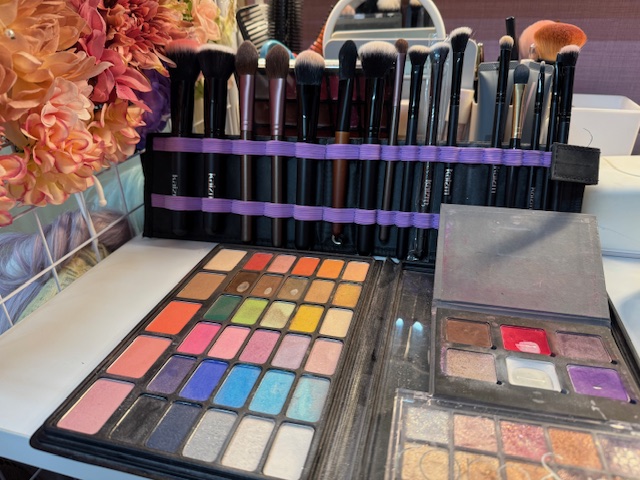 ドレッサーを写した写真。カラフルなアイシャドウパレットやふでが画面いっぱいにひろがっています。写真の左側にわ、かみかざりのお花が映り込んでいます