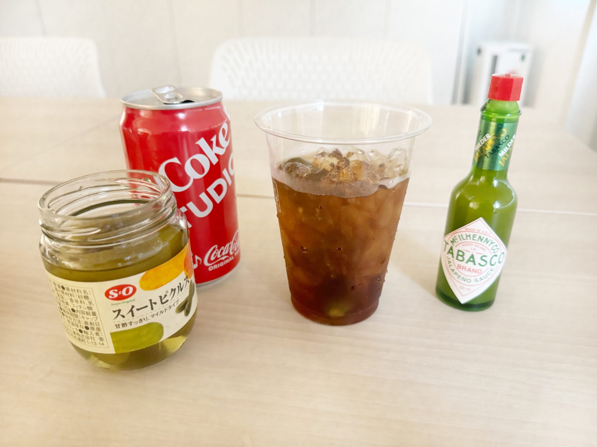 コンビニで購入したコーヒー用の氷に、通称デュアリパコーラをいれた写真。カップのまわりにわコーラの缶と瓶入りピクルス、ハラペーニョソースもならんでいます