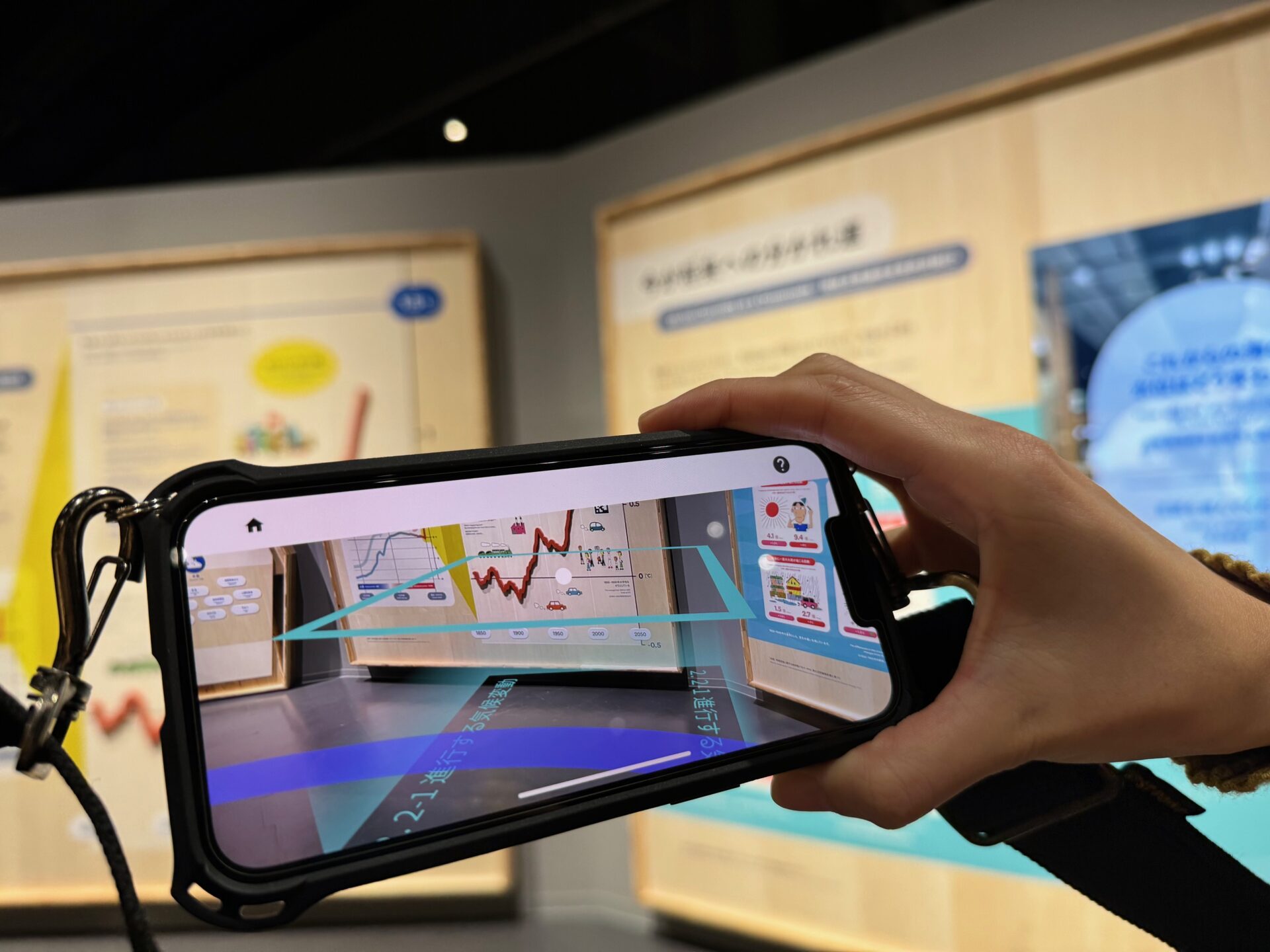 首からさげているスマートフォンと、そこに写された画面の写真。画面にはスマホのカメラを使うときのように対象ぶつが映し出されているほか、しかくいエリアの図が表示されています