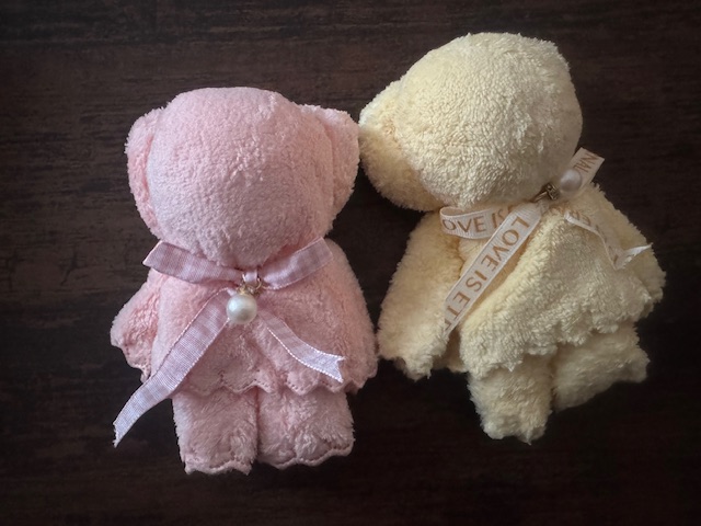 あわいいろあいの、ワンカラーのくまさんのかたちにおりたたまれたハンドタオルの写真。くびのところにリボンが結ばれており、ちょこんとパールがついています